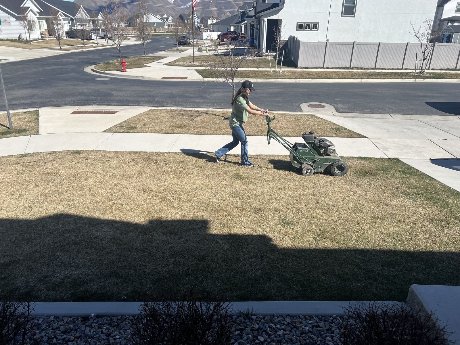 Lawn Doctor technician pushing an aerator across a front lawn in a Utah neighborhood.